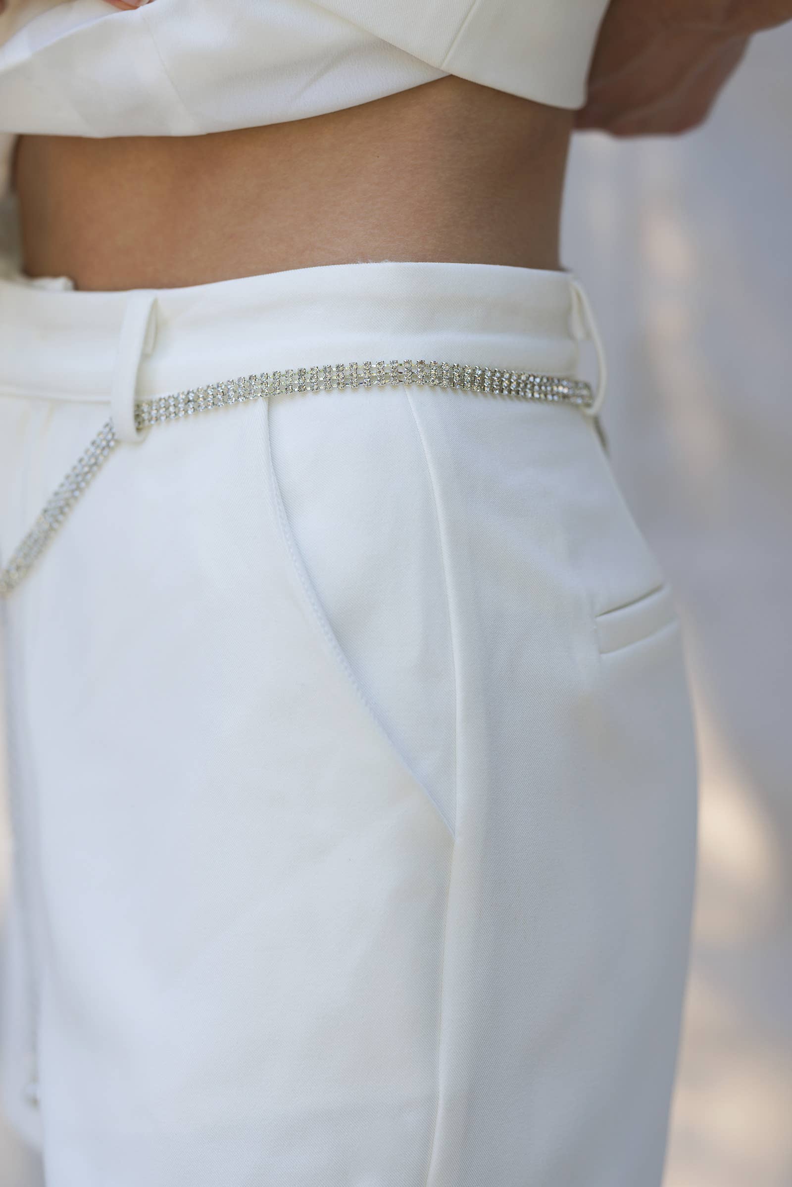 Close-up of tailored white pants featuring a stylish chain belt, ideal for women's boutique clothing and summer collection.
