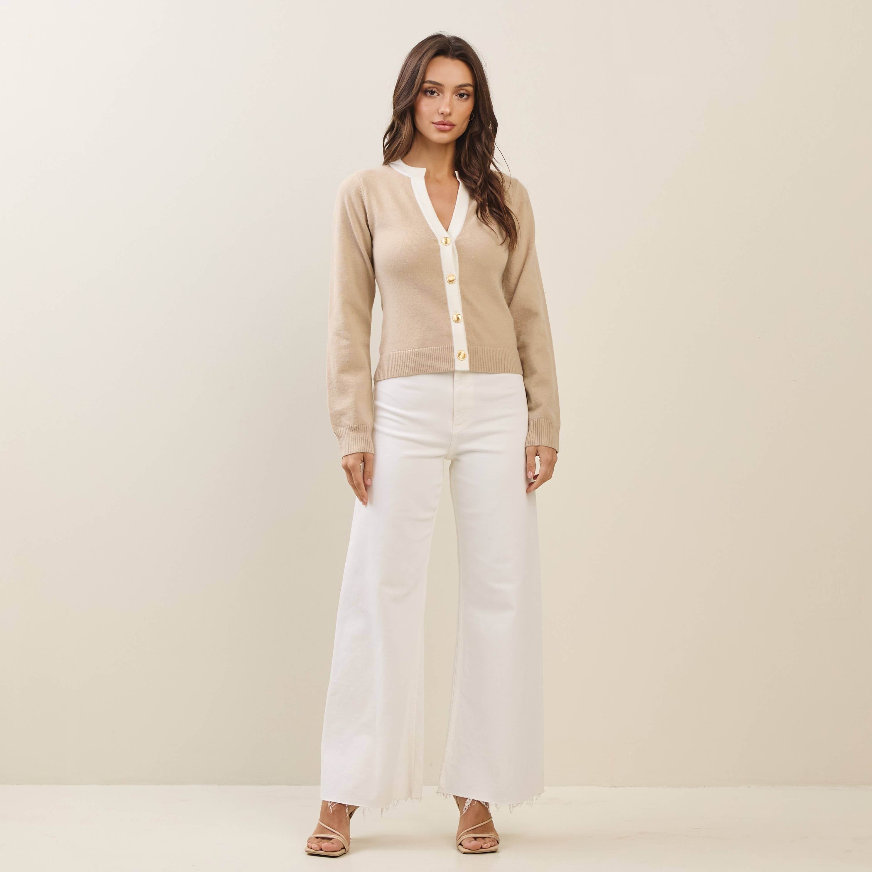 Model wearing a contrast taupe and white cardigan with gold buttons, paired with wide white pants. Women's boutique clothing.