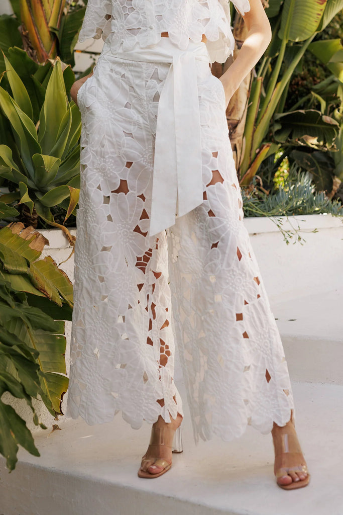 Elegant white wide-leg pants with lace cutouts, scallop hem, and belt. Perfect for women's boutique clothing and summer collection.