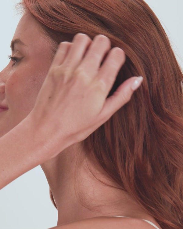 Woman with red hair styling her hair, showcasing a playful, elegant look. Perfect for summer boutique fashion.